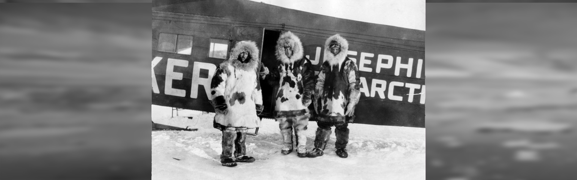 Three people bundled in thick fur coats standing outside of a plane in the snow