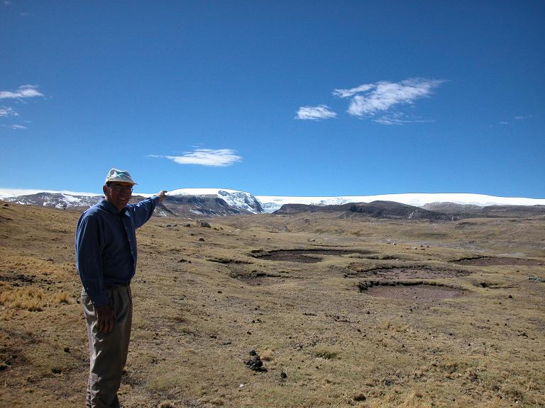 An person poses for a photo in Quelccaya, Peru. 2003. The landscape is green  until it turns snowy in the far off distance