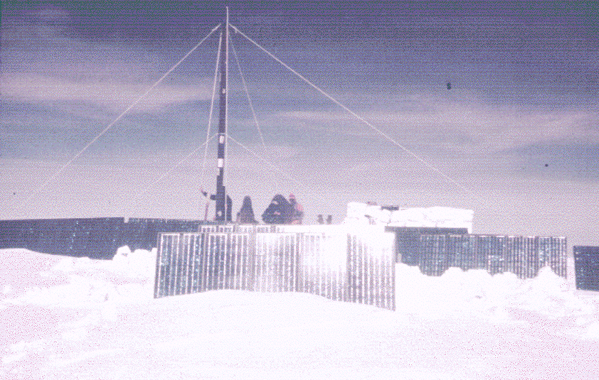 Ice core drill surrounded by solar panels on a snowy landscape.