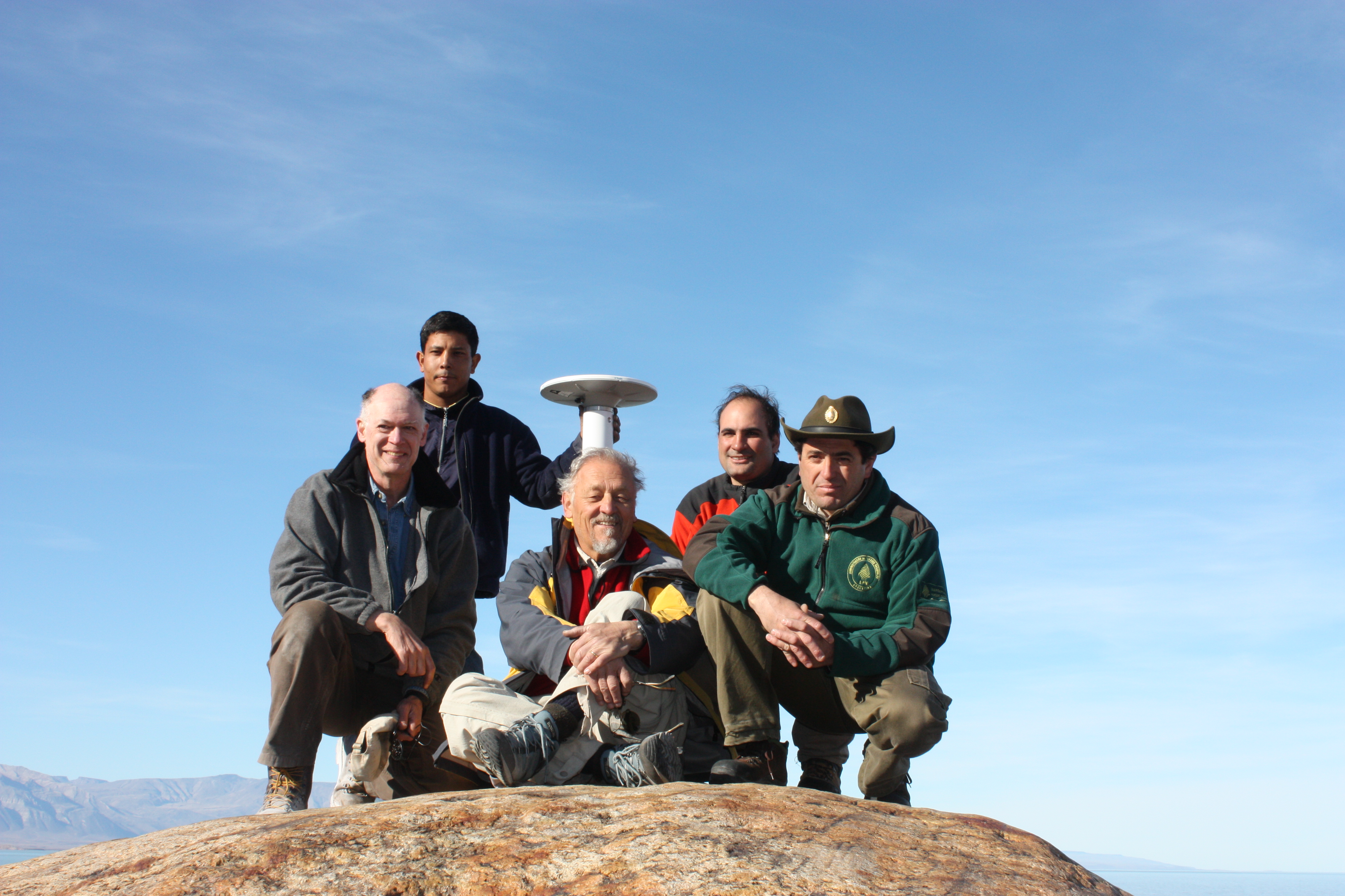 A group of 5 men crouched down on a hill with field equipment