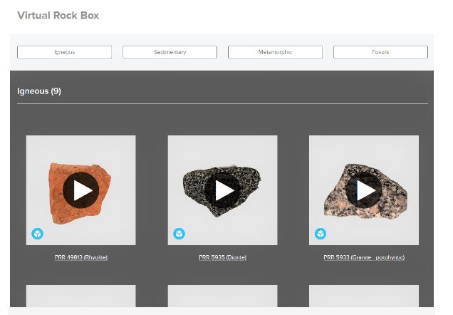An image of a screen showing the title of virtual Rock Box with 4 white buttons spaced out underneath it with light grey background . White boxes have writing Igneous, Sedimentary, Metamorphic and fossil. Underneath is a dark grey background with Igneous(9) written in white text as if selected then under that   with three rocks each in it's own square white box and a play button on each, showing it is an interactive page.
