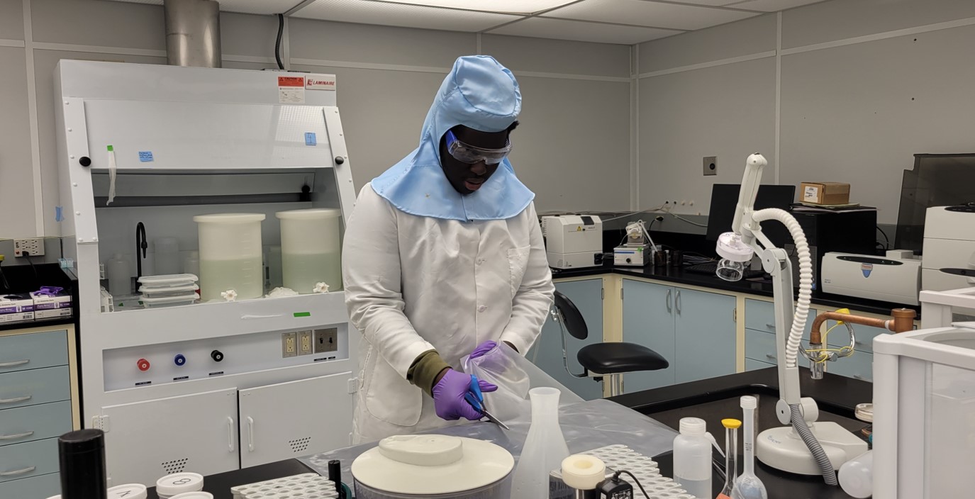 Student is full gear including head cover and googles working with lab equipment in clean room