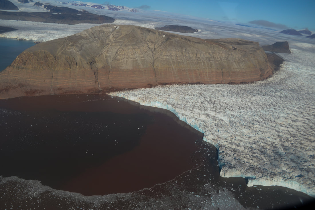 A rocky mountain, snow and ice and water under blue skies.