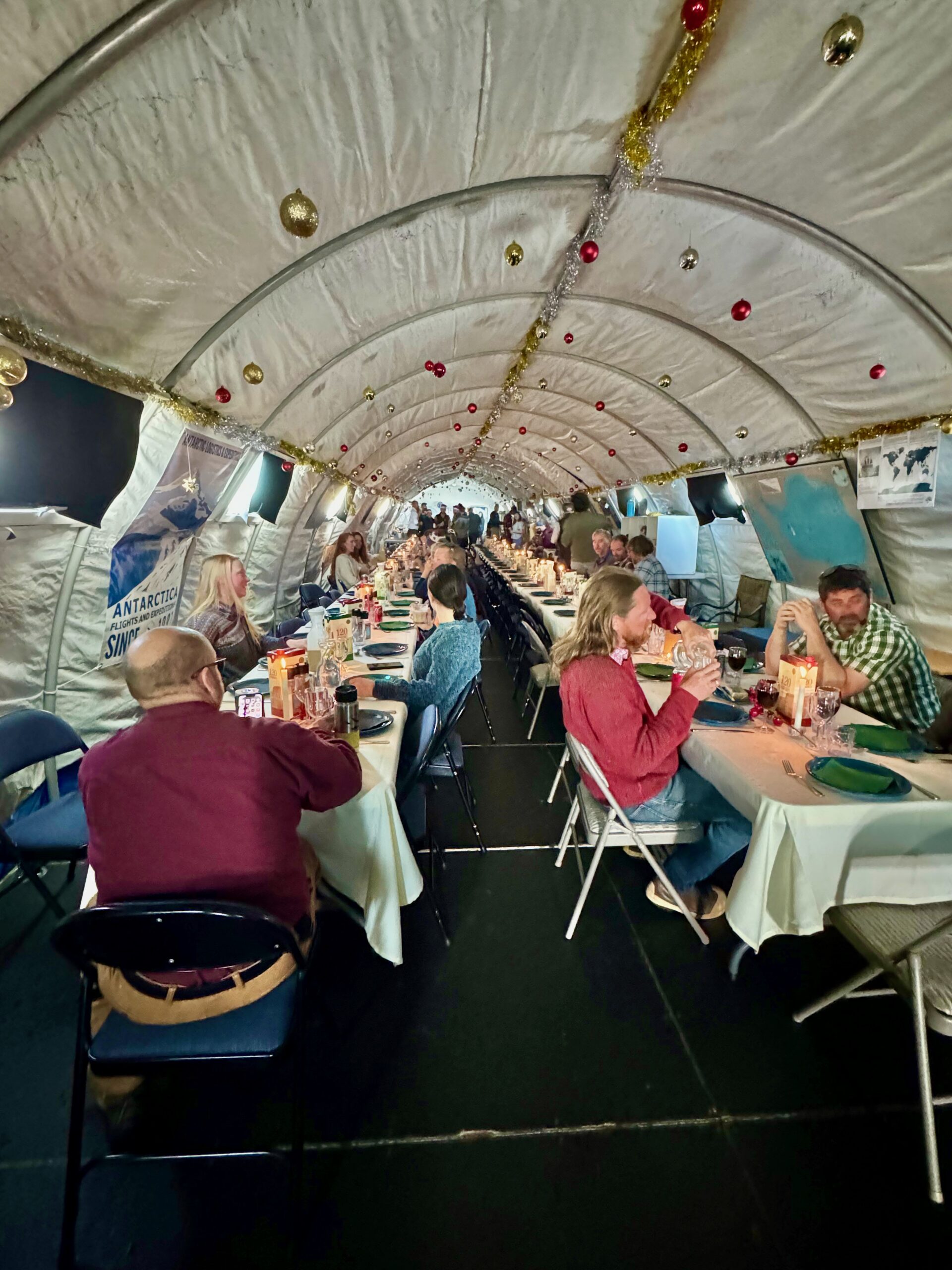 People sitting at two long tables in a tent with holiday decorations.