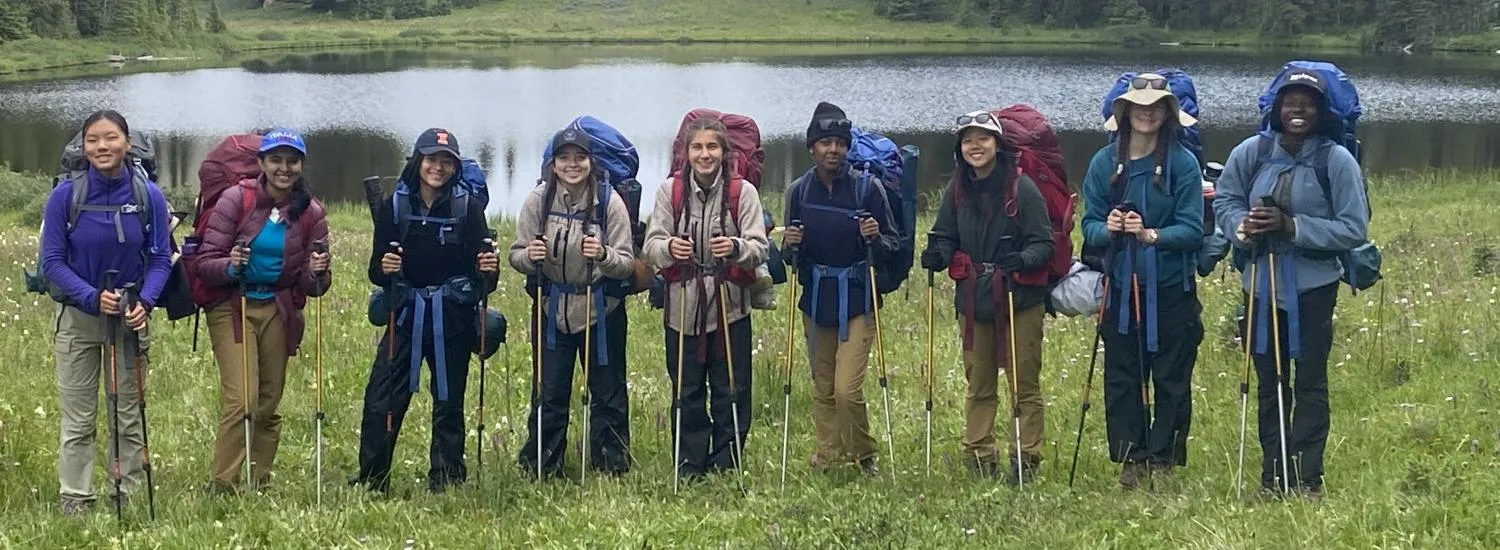 A group dressed in climbing gear posing for the picture outdoors in a field in front of a pond.