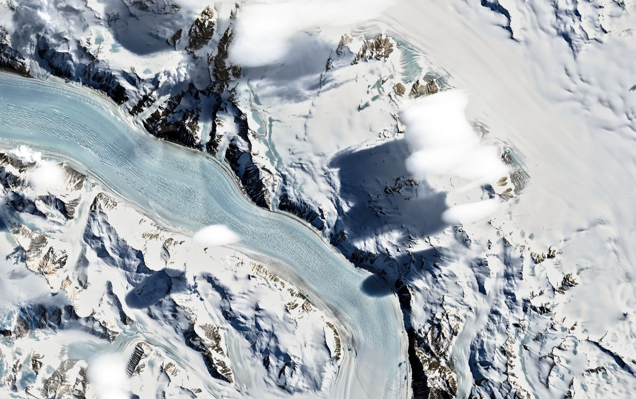 Close-up aerial view of glaciers, snow-covered mountains and white, puffy clouds.