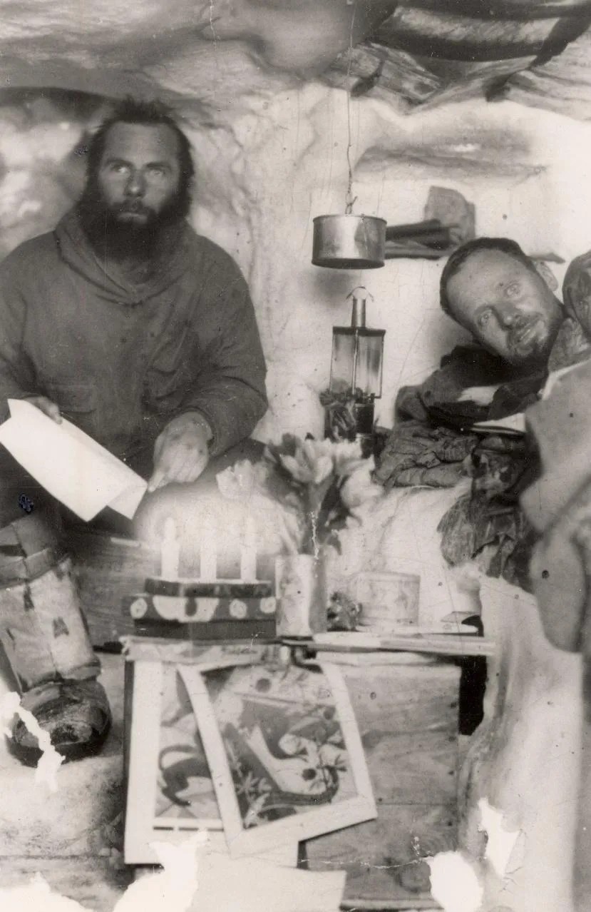 Black and white pic of two men in an igloo with their supplies.