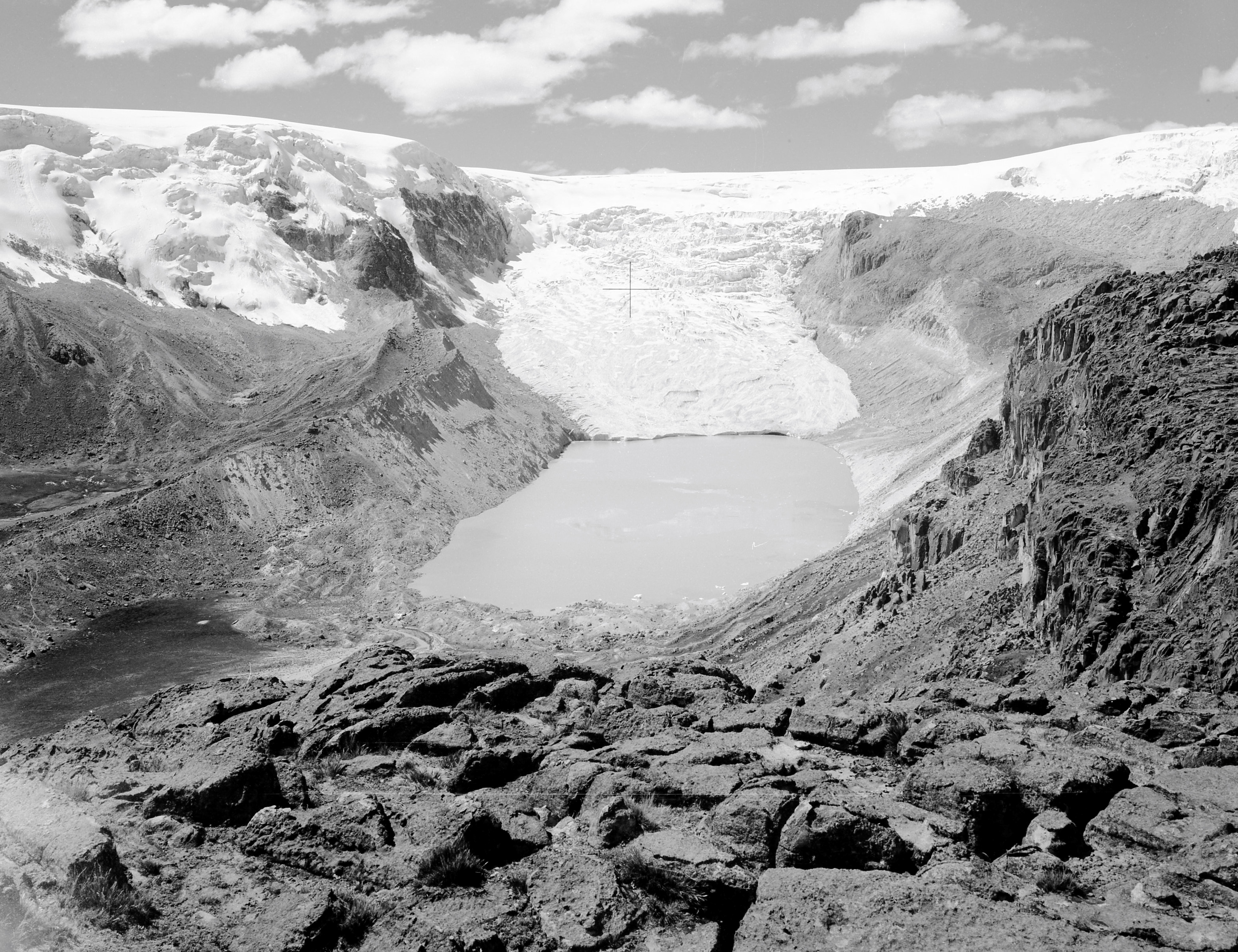 A black and white image of a glacier with a lake in a rocky terrain.