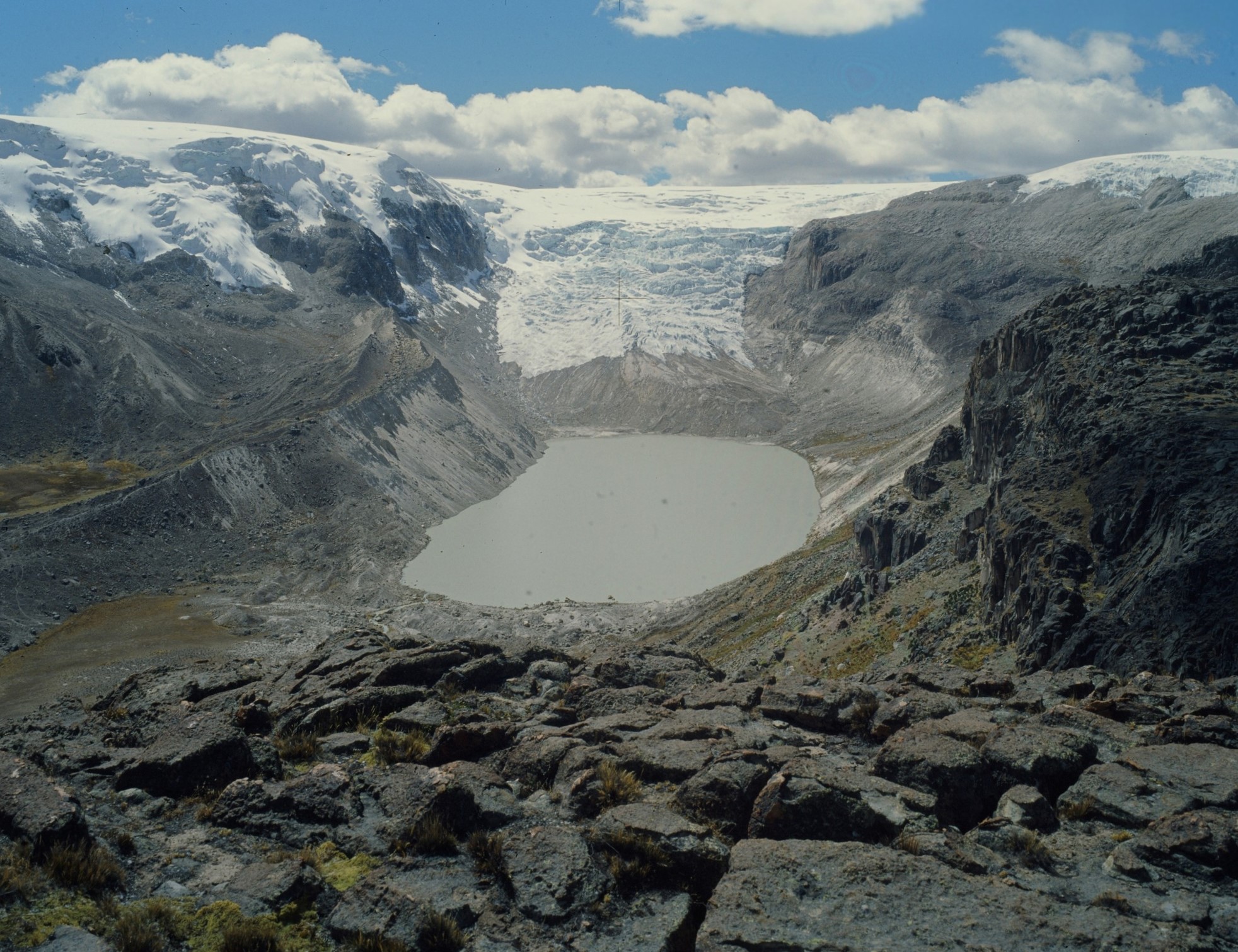 A glacier with a lake in a rocky terrain with white cloud.