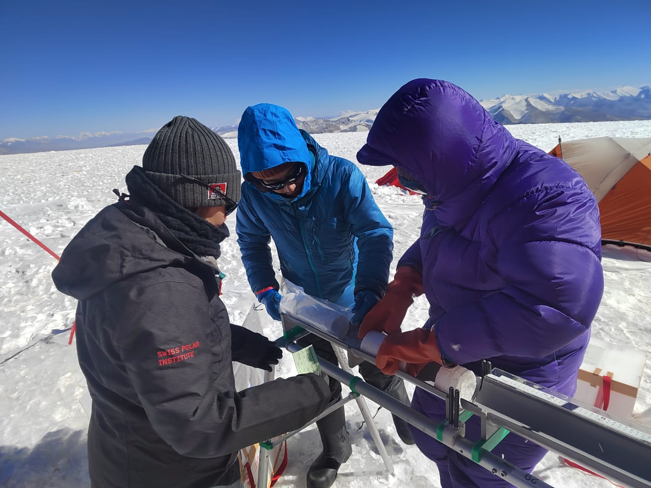 Three scientists with an ice core on a table in the field.