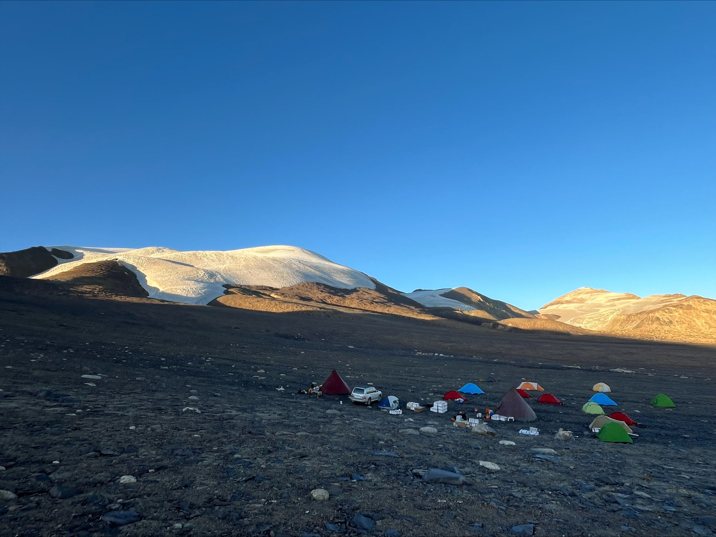 Colorful base-camp tents below glacier slopes in low-angle light.