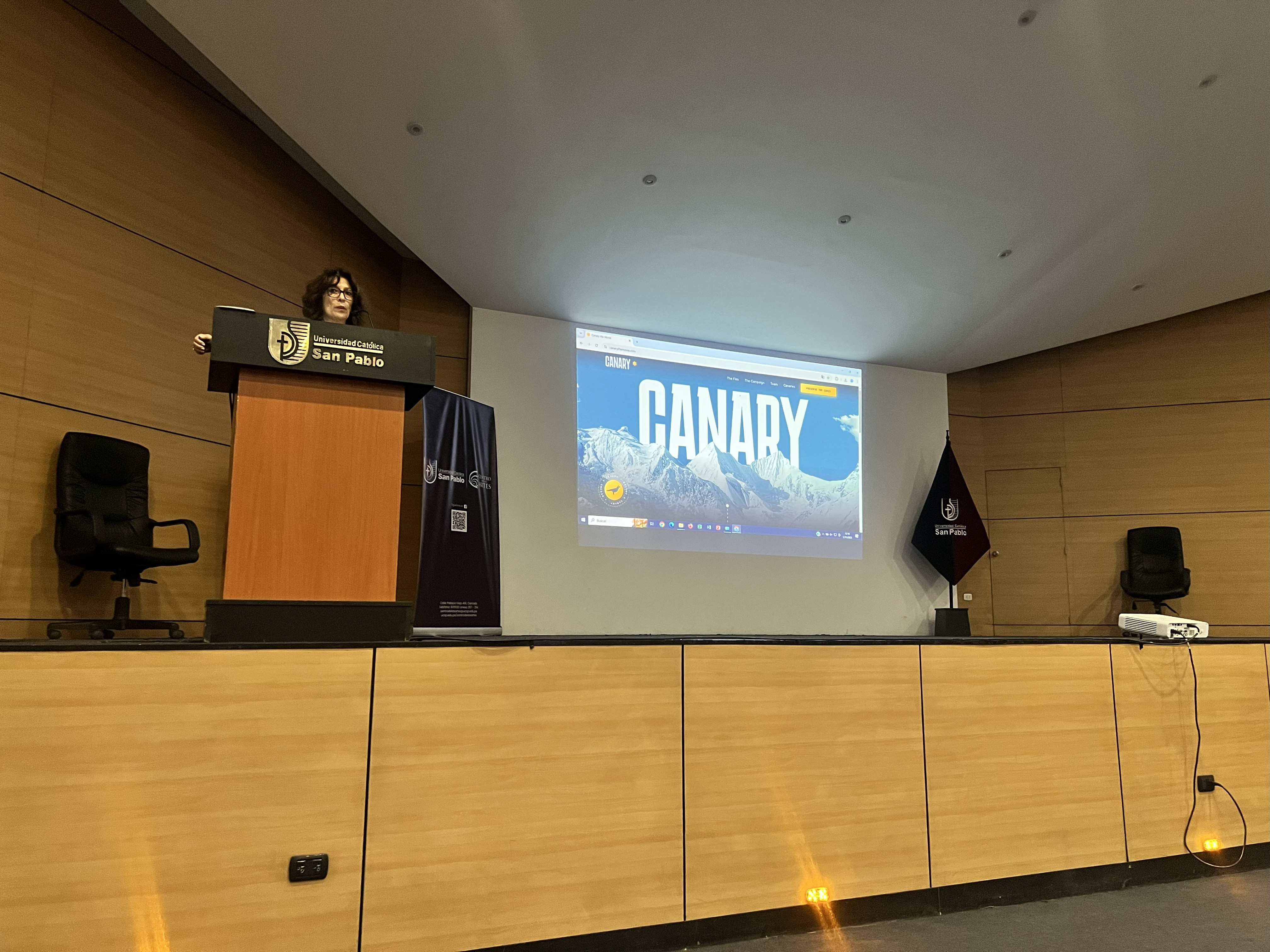 Speaker at a podium at Universidad Católica San Pablo with a projected “Canary” presentation on the screen.