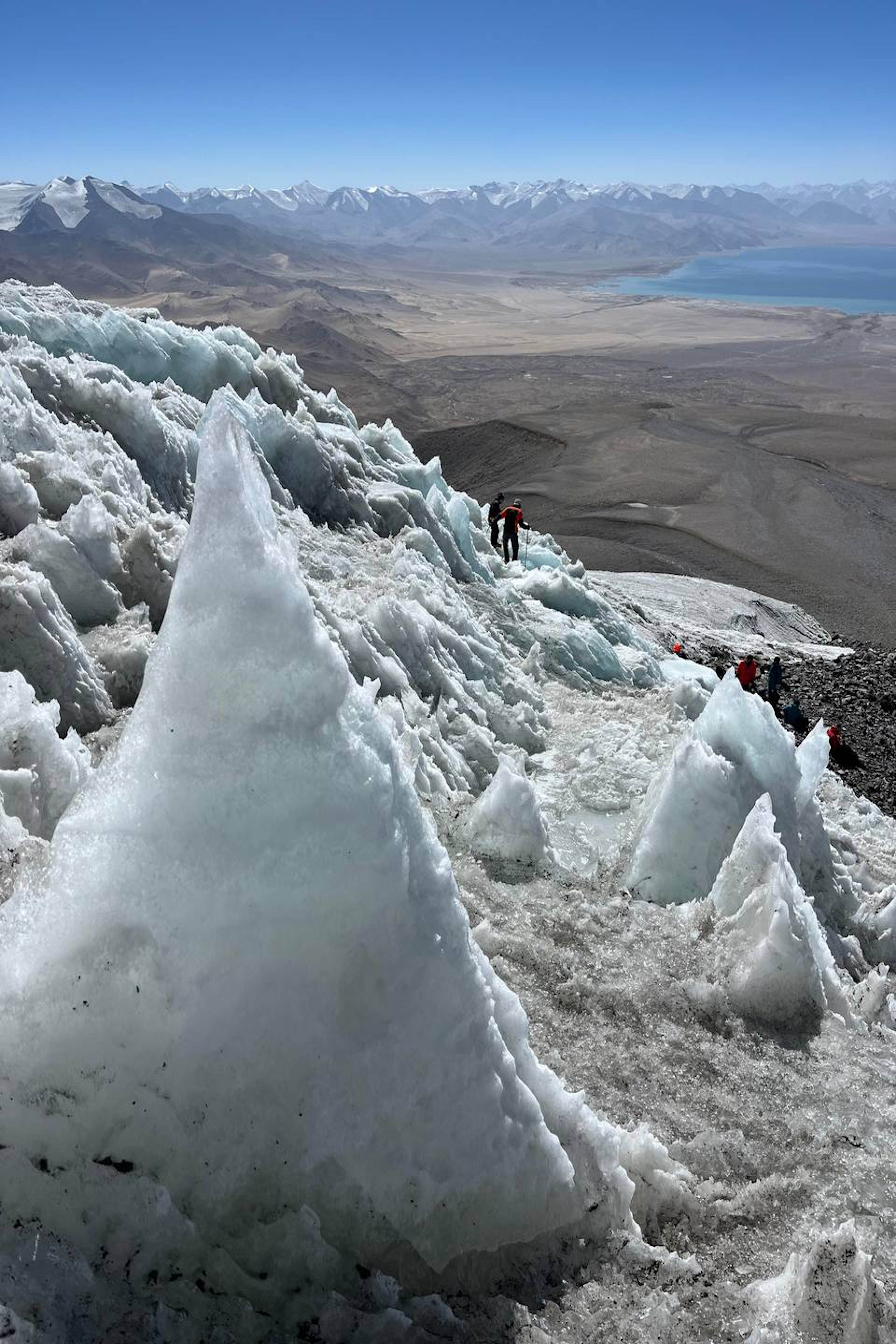 A view from the top of a glacier, looking down at hikers and a valley 