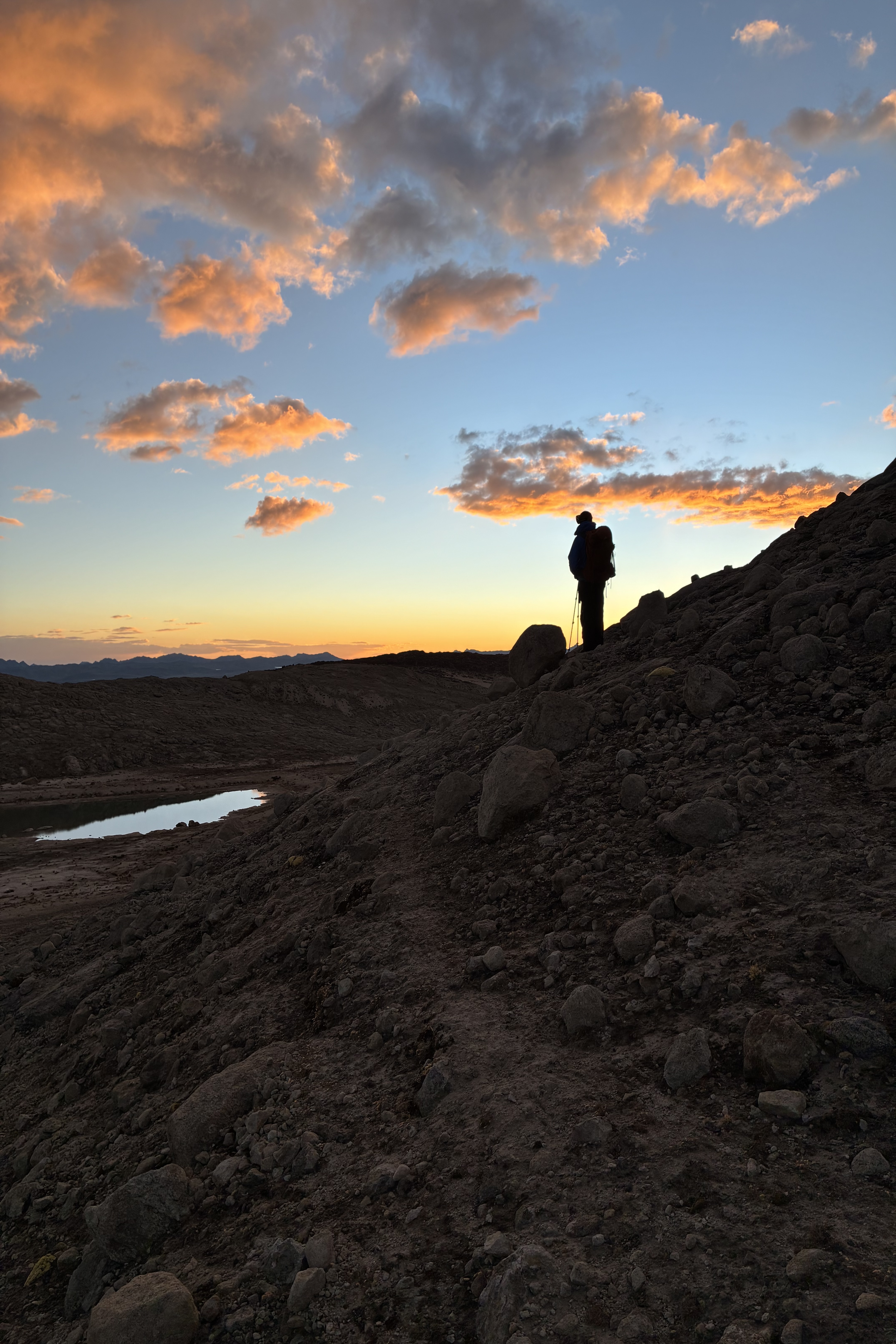 A silhouette stands on the edge of a trail looking out to a pick and yellow sky