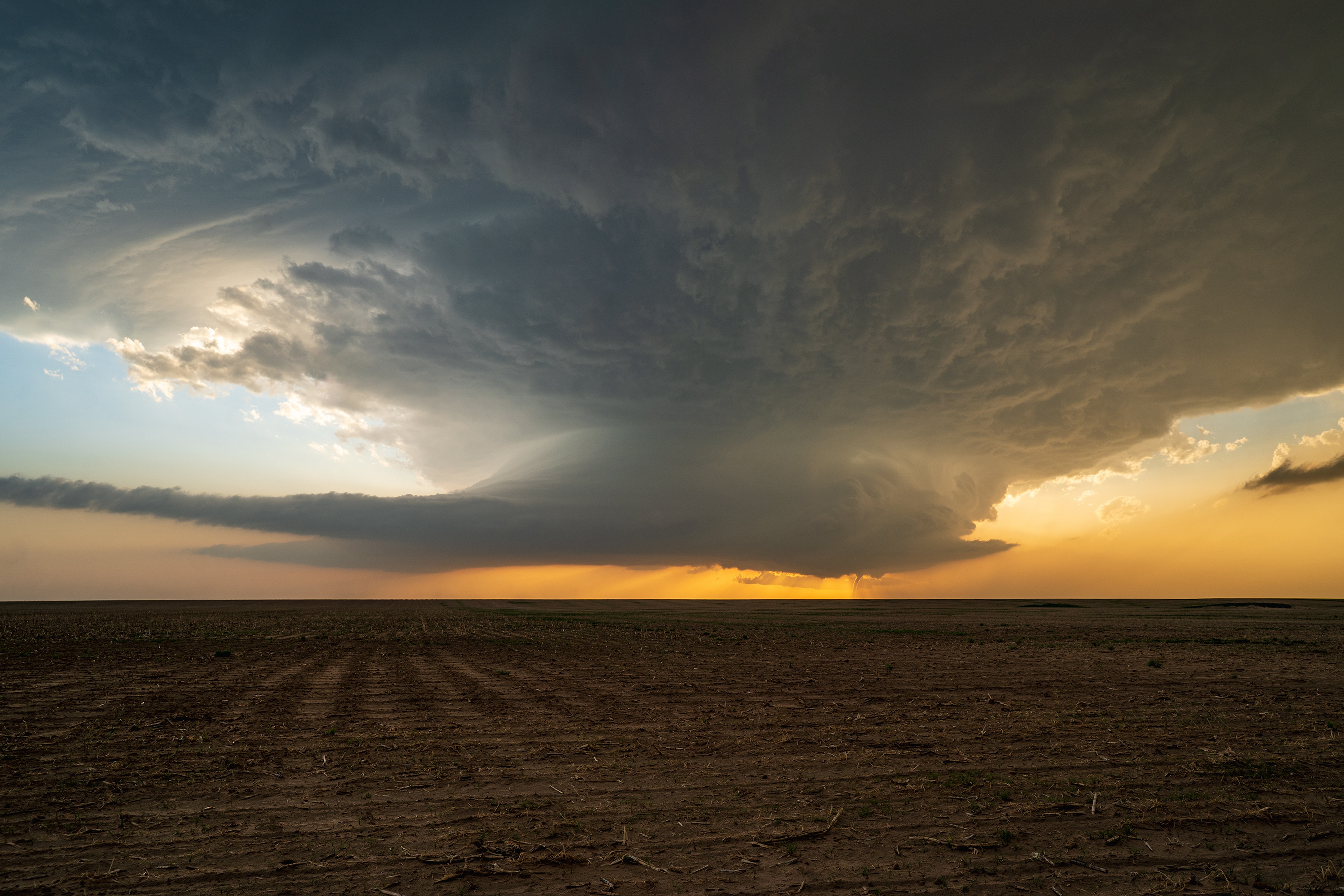 A funnel-shaped tornado touches down on an open plain beneath a large, dark storm cloud.