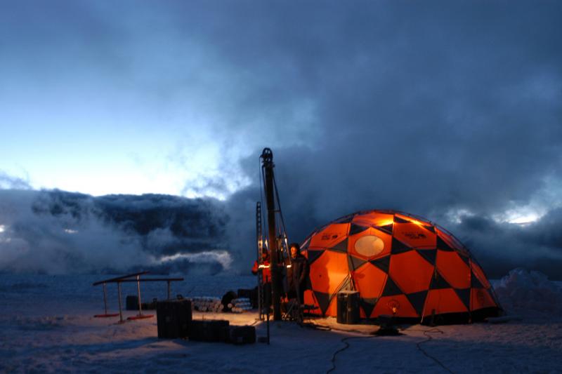 Ice core drilling at night. the landscape is dark except for a lit up shelter 