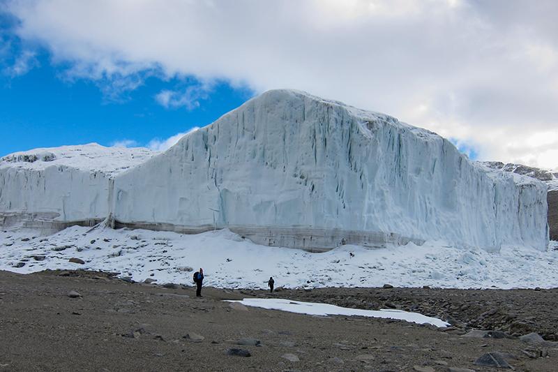 Two people walking towards large glacier