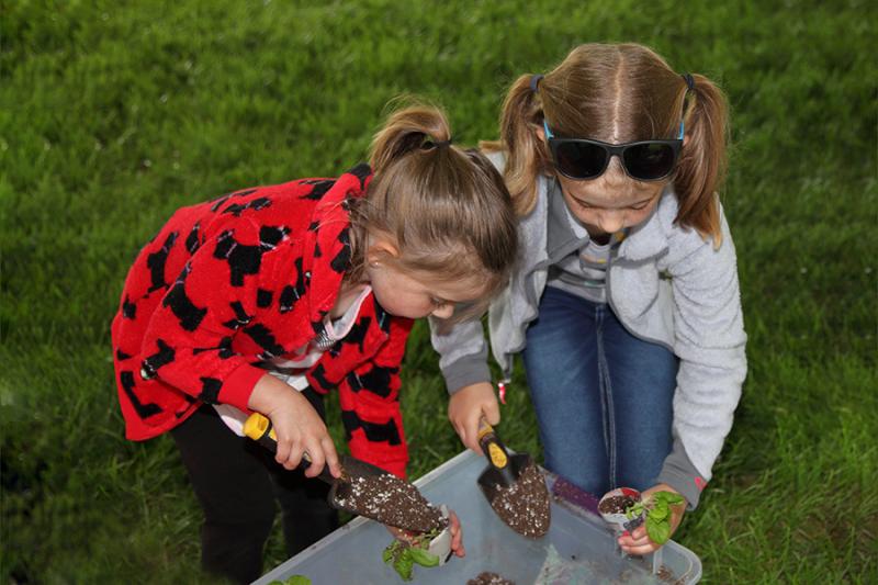Two children standing over a container carefully shoveling dirt into plant containters