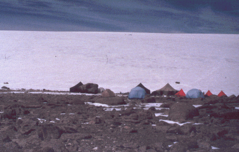 Dunde Ice Cap, China. Small colored tents are positioned on the rocky landscape next to the water