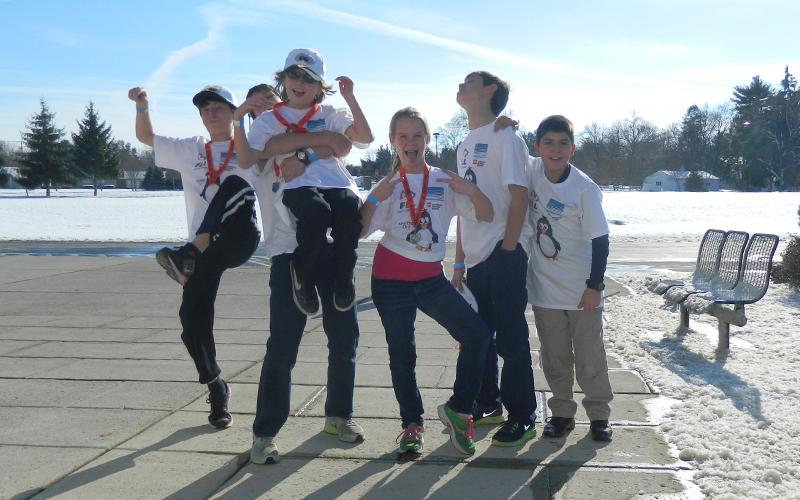 young students pose for a photo outside the Byrd Polar and Climate Center.  They are wearing matching white T-Shirts and there is snow all around them 