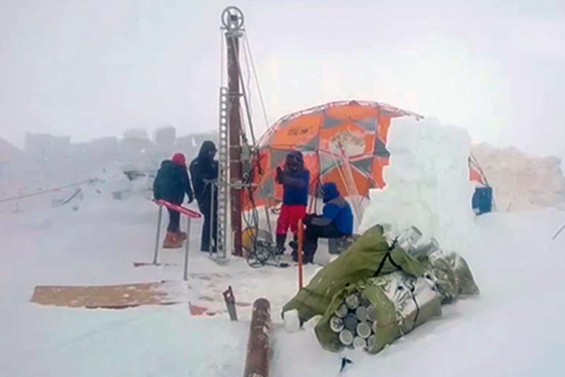 Surrounded by snow, four scientists drill ice cores from the glacier using a tall machine that towers over them