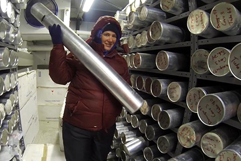 A scientist holding an ice core cyllander inside the ice core storage freezer. There are dozens of cyllanders stored on the shelves.