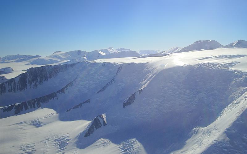 a snowy, rocky landscape brightly reflect the sunlight. The sky is clear and blue 