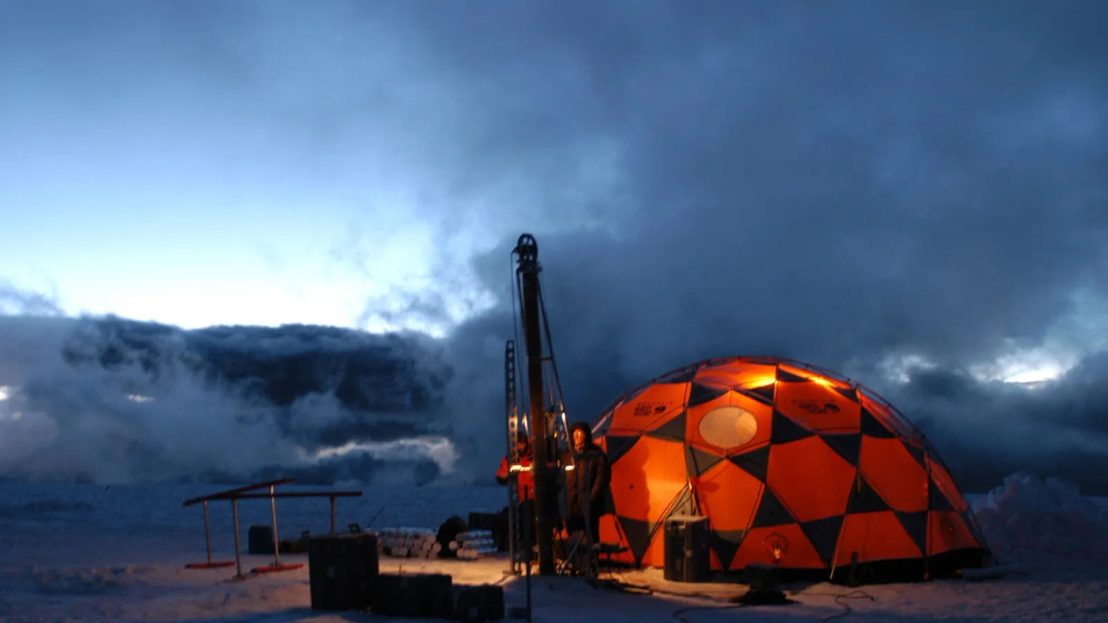 Ice core drilling at night. the landscape is dark except for a lit up shelter 