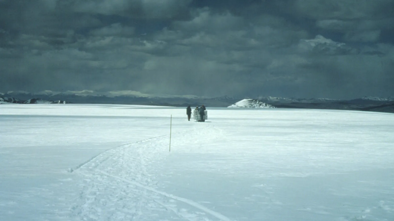 People walking in a distance in a snow covered field under gray, cloudy skies.
