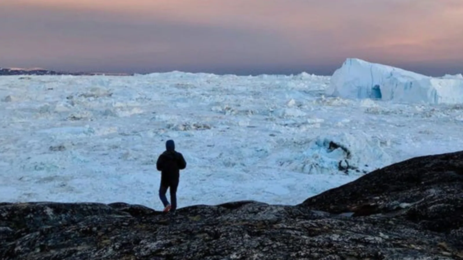 A silhouette of a person walking into the arctic landscape. The ground is snowy and icy 