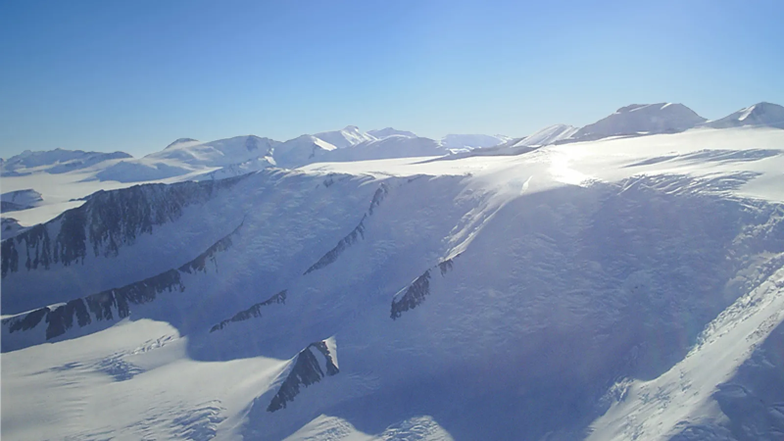 a snowy, rocky landscape brightly reflect the sunlight. The sky is clear and blue 