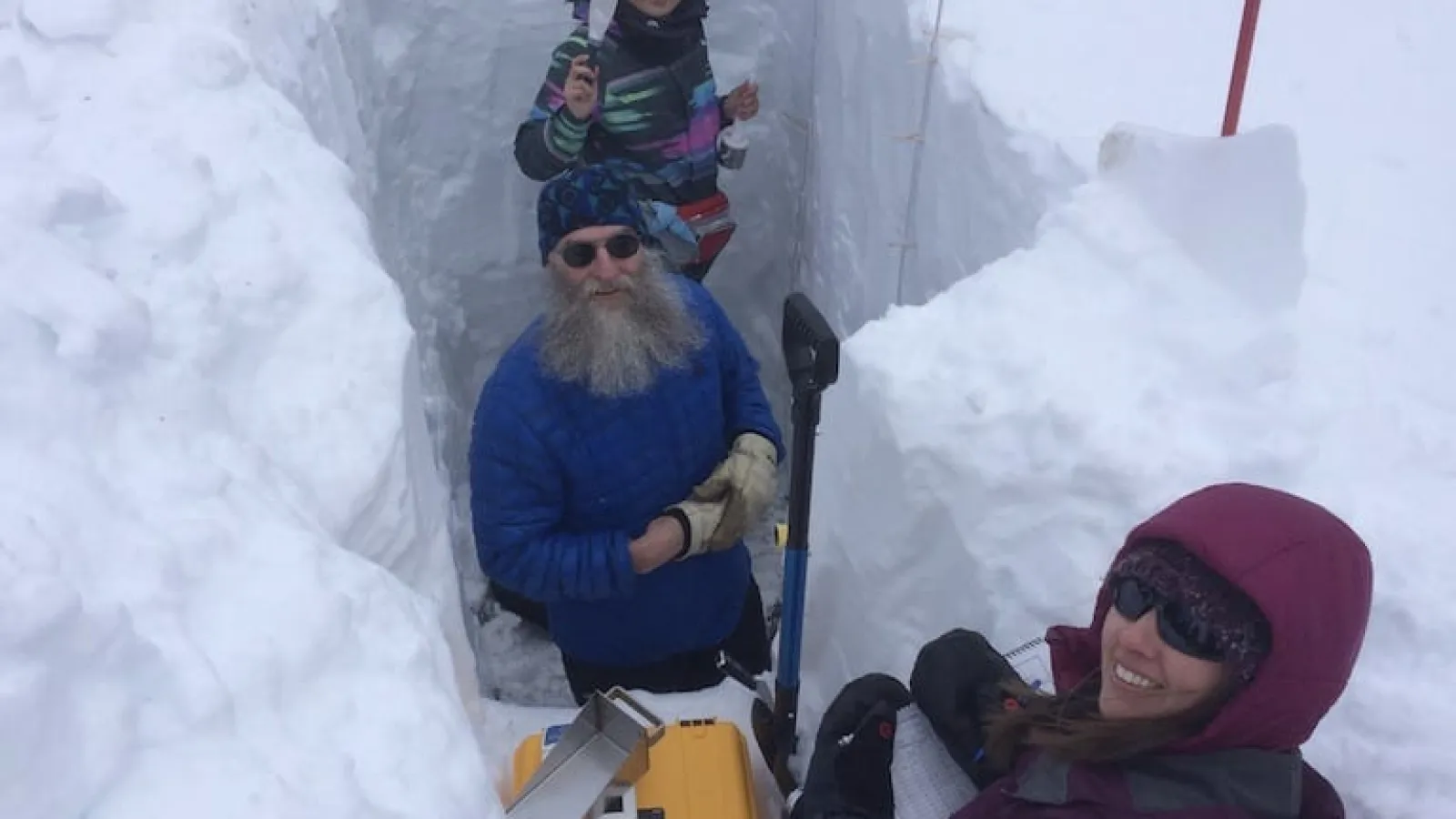 Three people posing for a photo as the stand in a large cutout of ice in the ground.