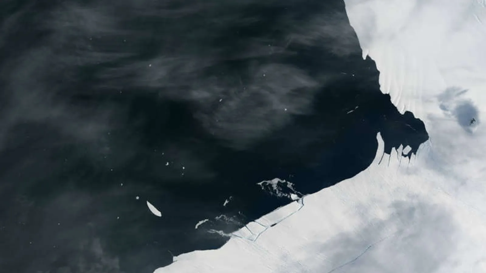 Aerial view of an icy shoreline against a dark blue body of water 