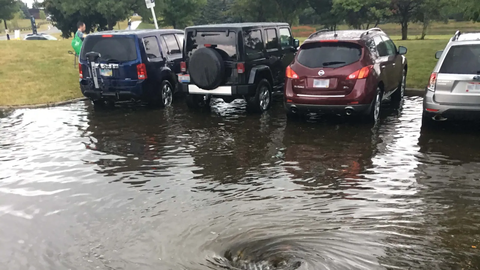 A parking lot is flooded with rainwater and four parked cars. 