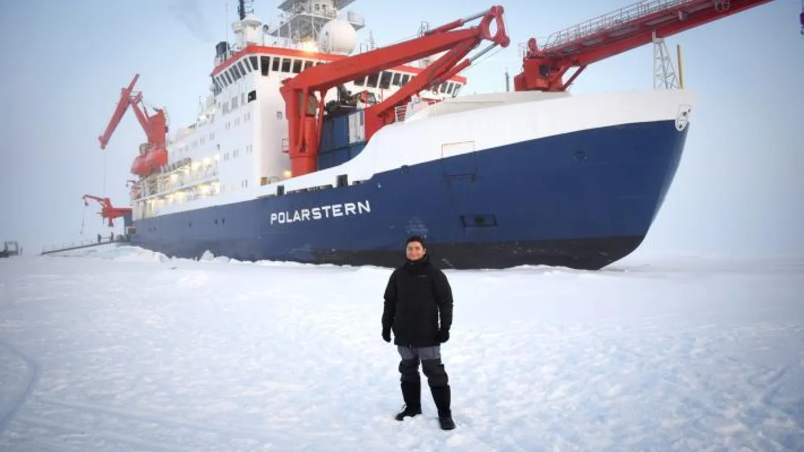 Individual poses for a photo in front of a large ship in a snowy landscape 
