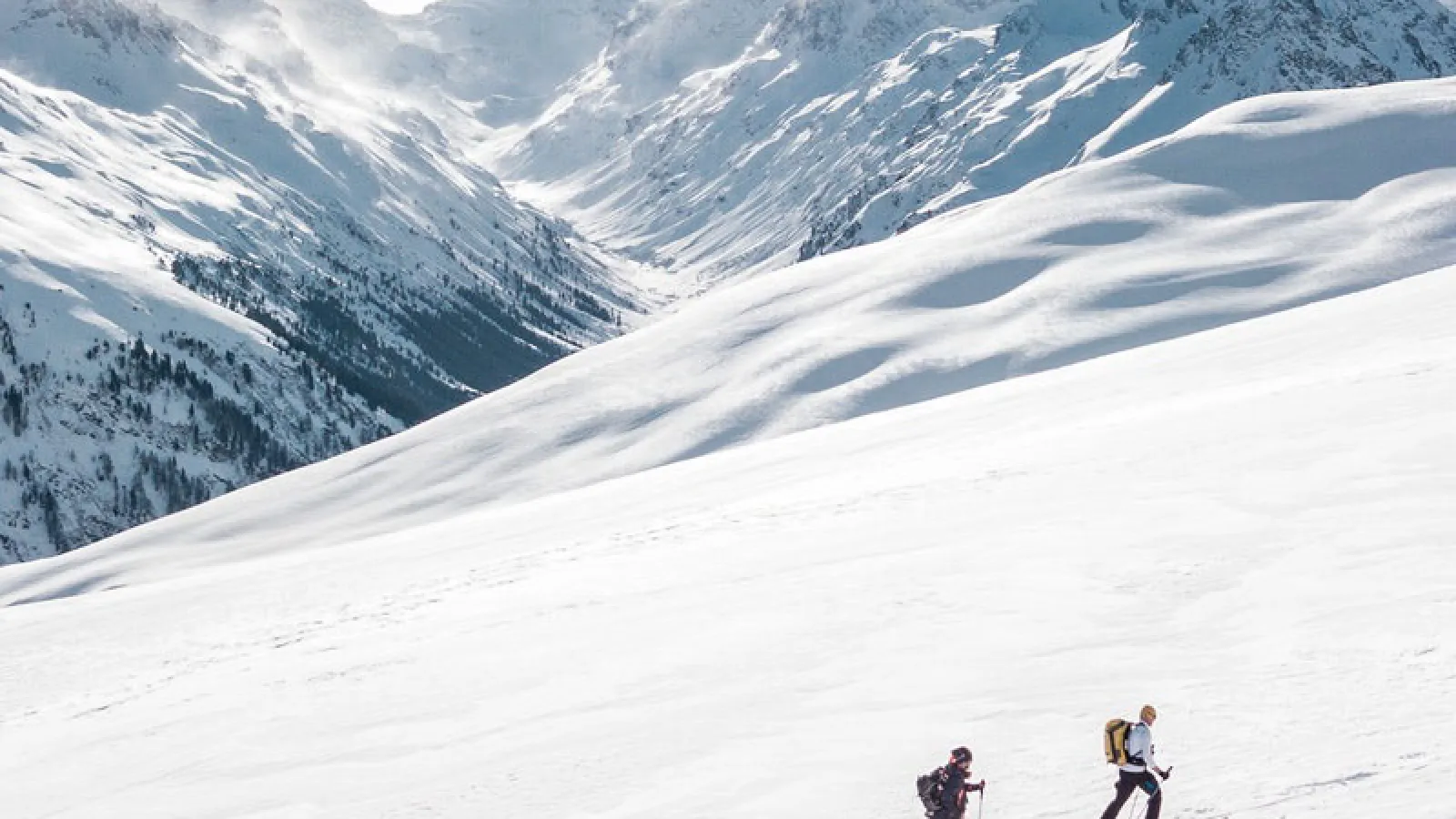 Two mountain climbers ascending on a sunny day with snow covered mountains.