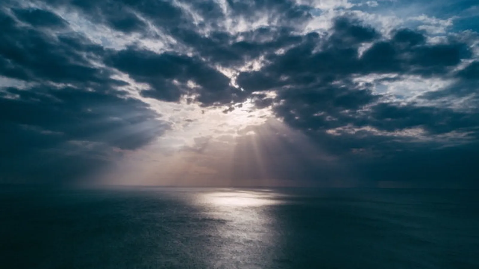 calm ocean under dark clouds with sunlight coming through