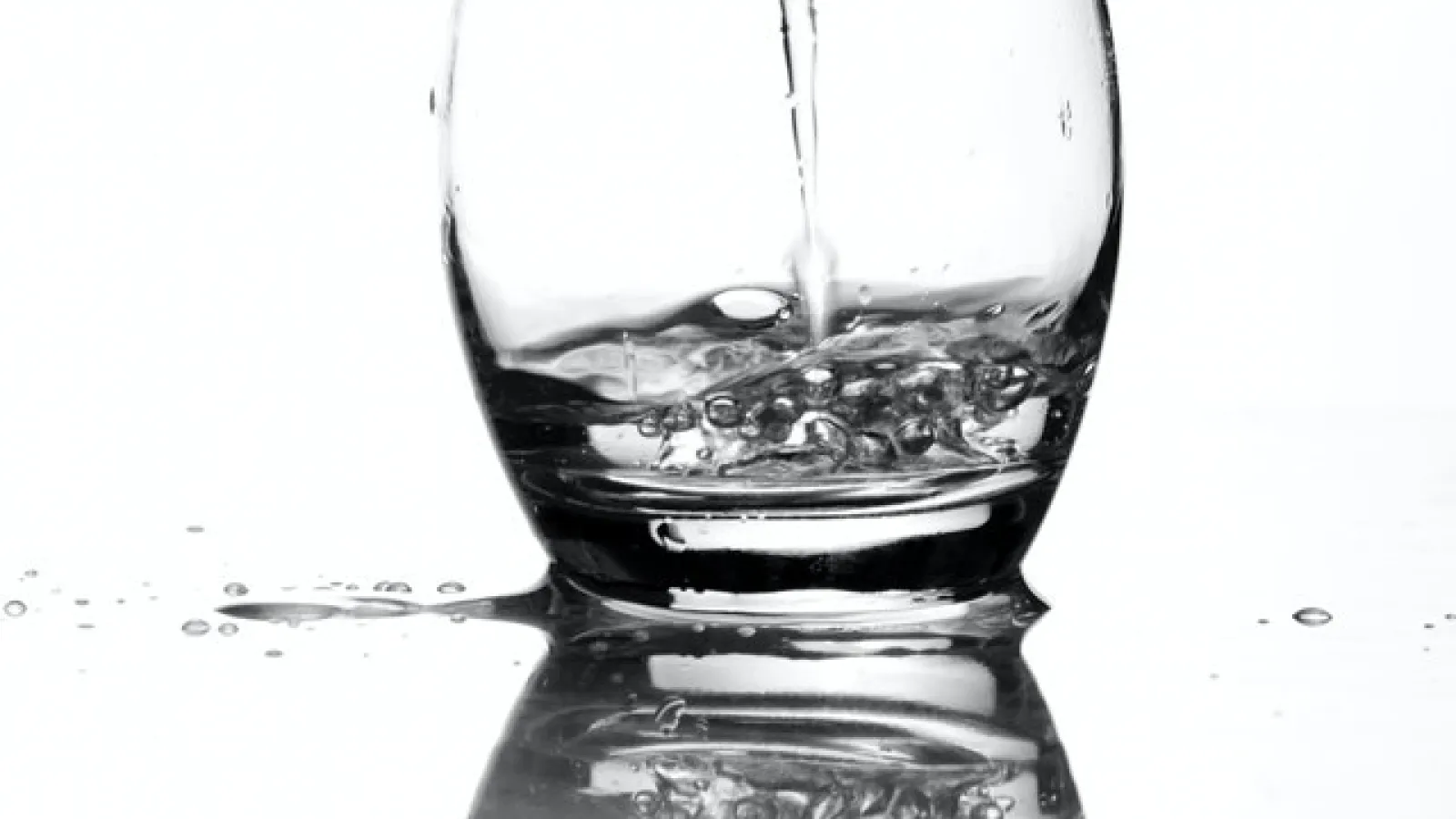 water streaming into a short Glass cup with a white background and cup reflection visible 