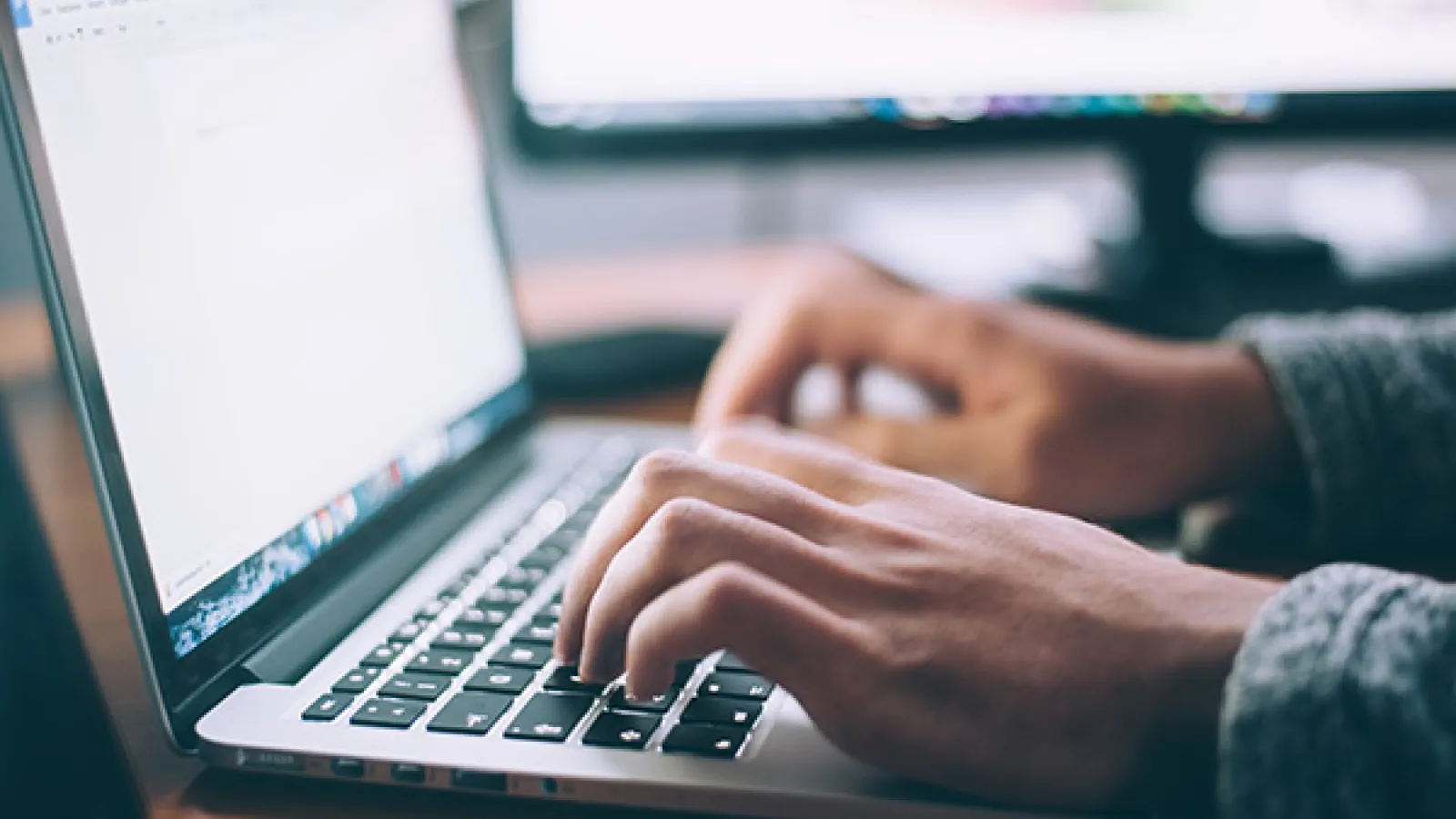 stock photo of two hands typing on computer. The screen of the computer is bright white. 