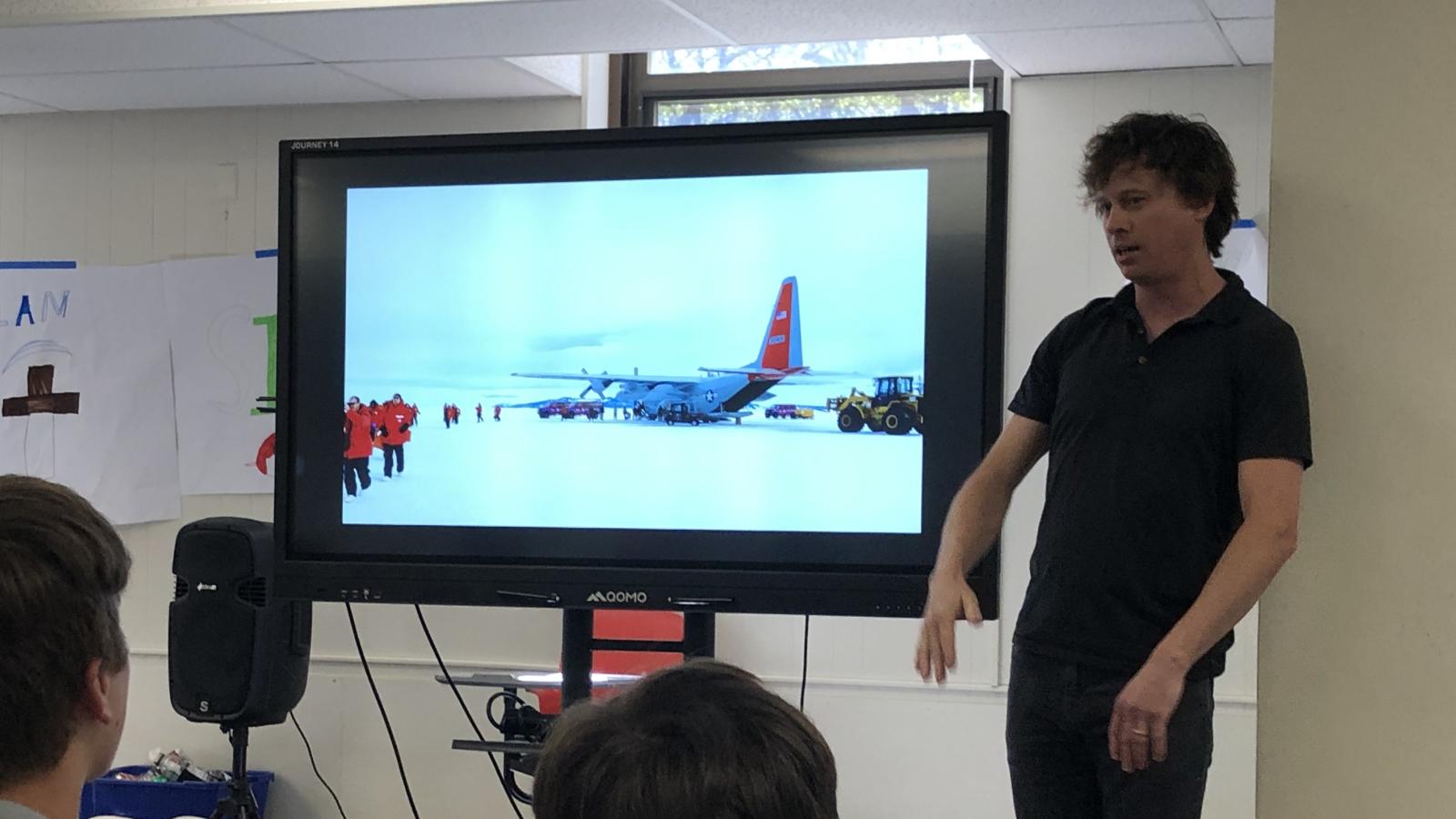 researcher presenting to students with a video display showing Antarctica.