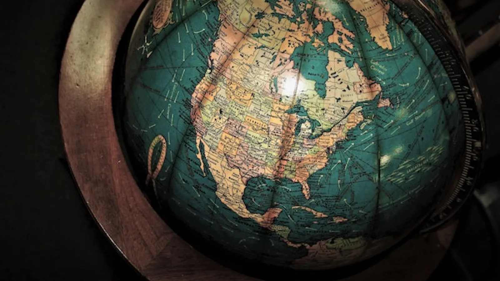 Image of partial globe focused on north America in light tan color and oceans in green on a dark wood frame with dark background