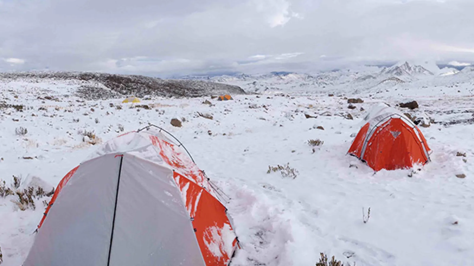 Red and gray tents in snowy research site. The landscape is snowy and rocky with gray skies.