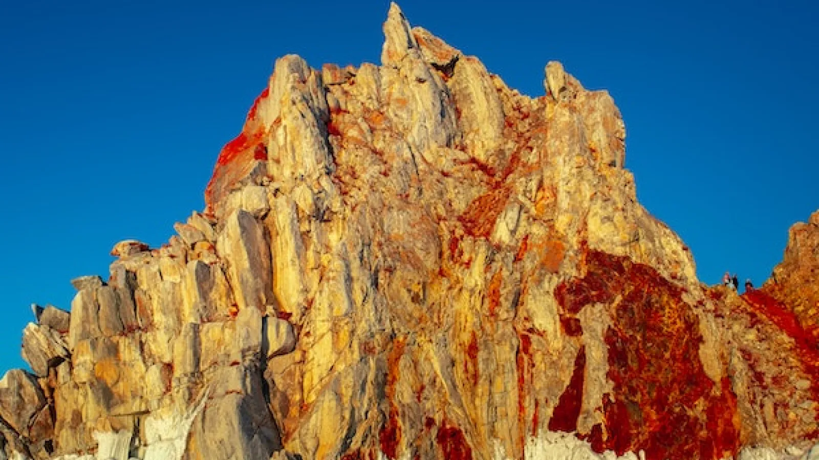 Sharman Rock in Siberia Russia yellow jagged rocky mountain with read streaks against light blue sky