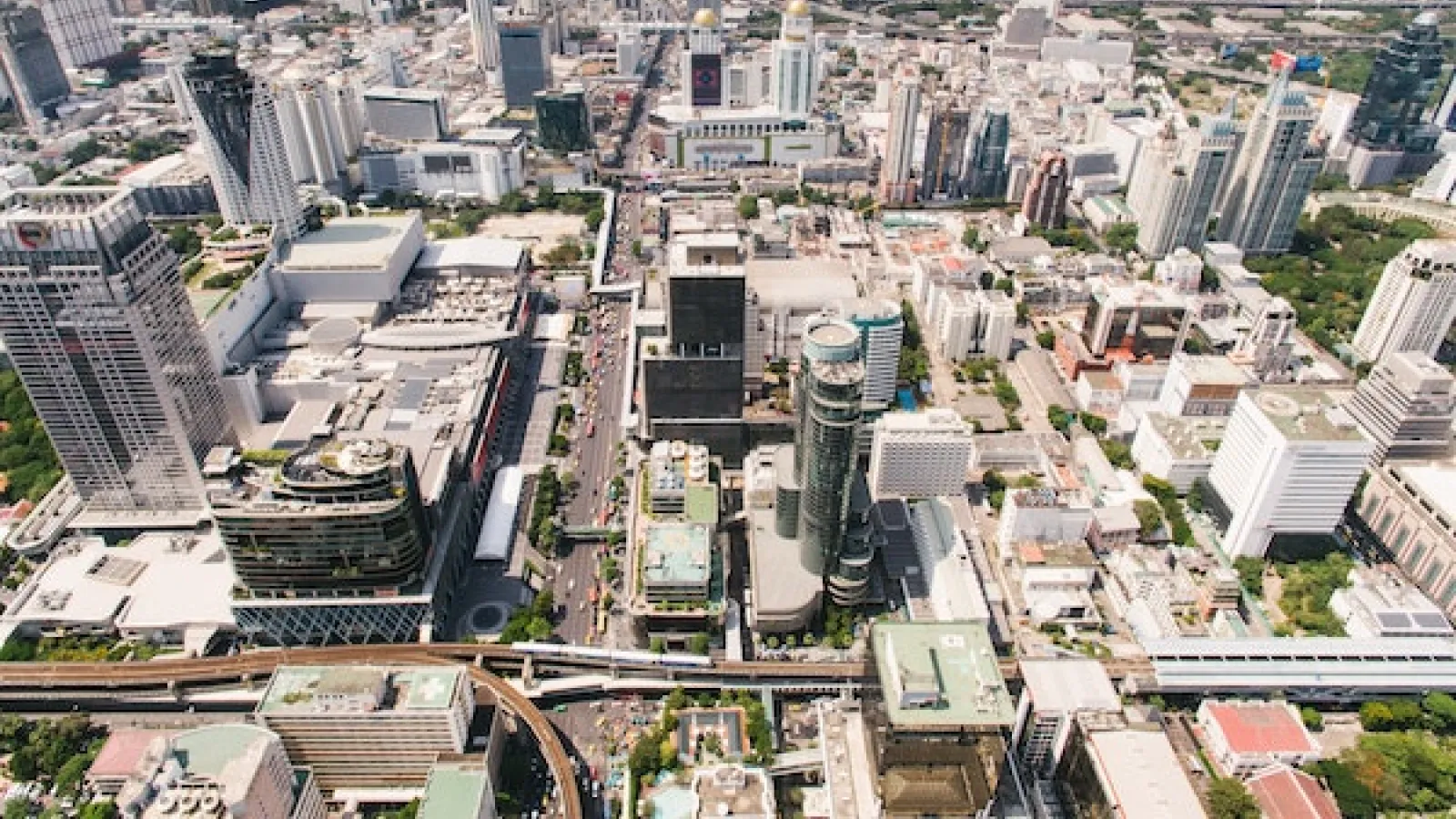 A day time bird's eye view of a large city with tall buildings, freeways, streets and some green space sprinkled in. Buildings fill the image with some smog cover. 