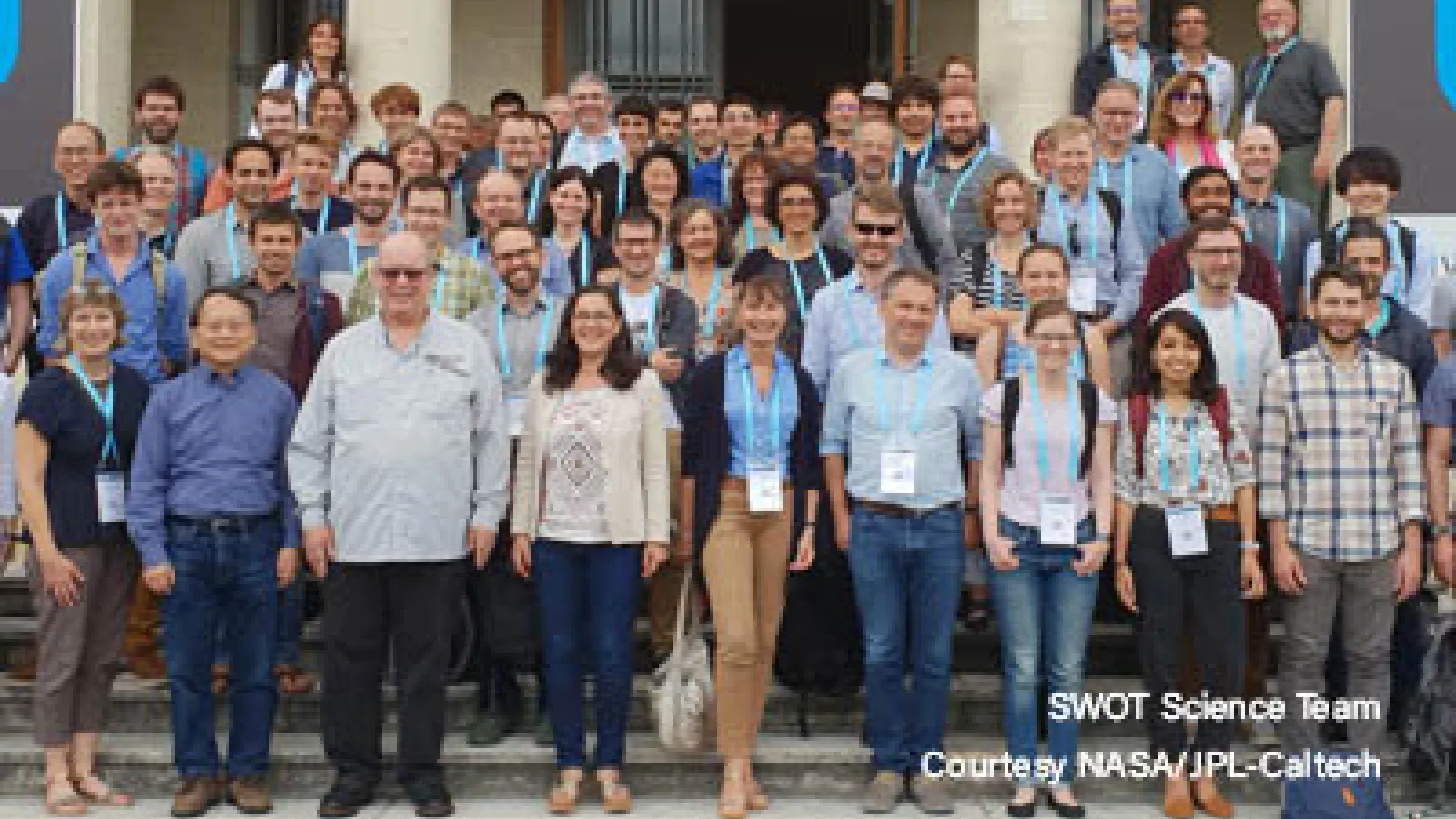 A group of 20+ scientists that work on the SWOT mission standing outside a building on steps posing for an image. 