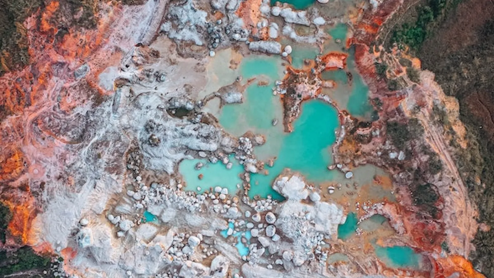 A mine from above with aqua water and clay and some white color earth and some vegetation.