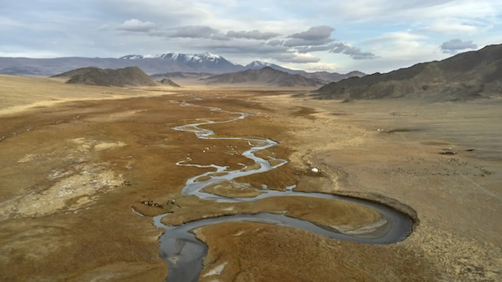 River rolling through a brown valley with short brown vegetation along the river 