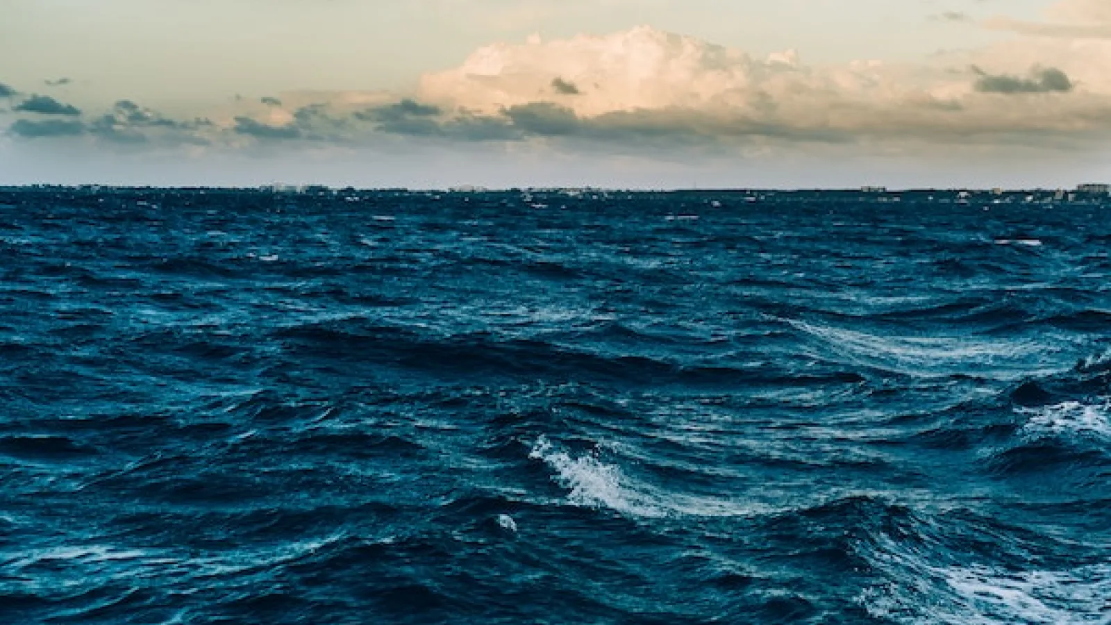 Surface view of calm open water under a white blue sky with clouds