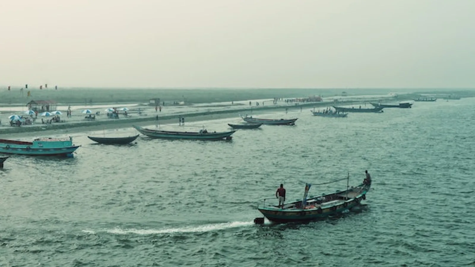 Boat traveling in calm open water with other boats of different sizes anchored in a row in the water