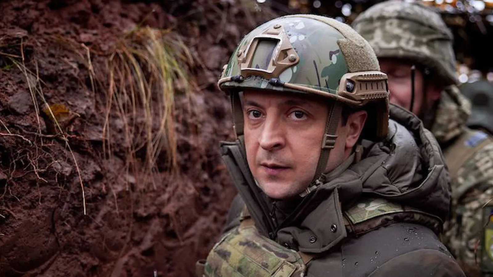 A soldier in combat gear in a muddy trench. There is another soldier behind him.